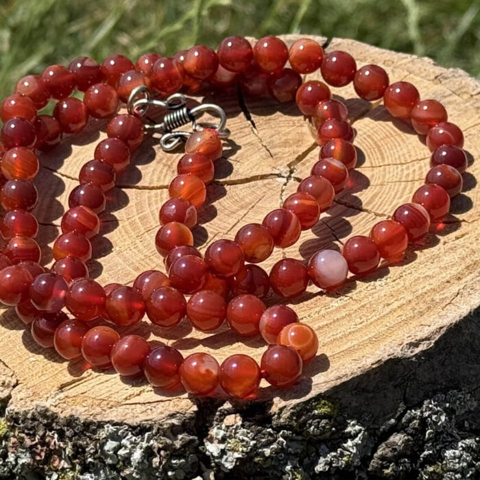 Carnelian crystal necklace resting on wooden block with garden grass and foliage background