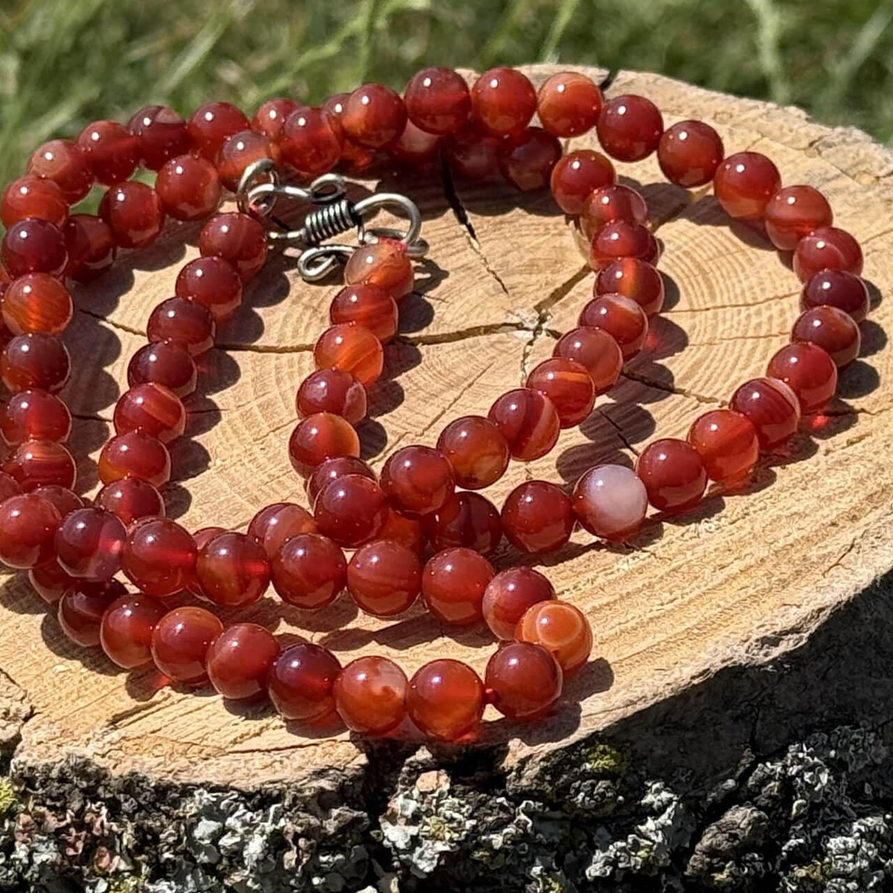 Carnelian crystal necklace resting on wooden block with garden grass and foliage background