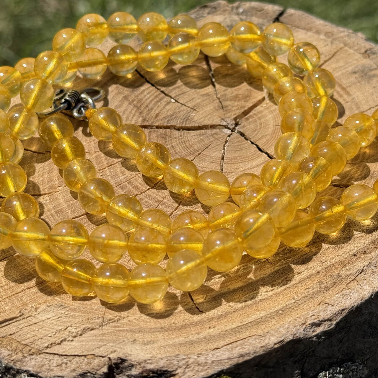 Citrine crystal necklace displayed on wooden block with garden grass and foliage background