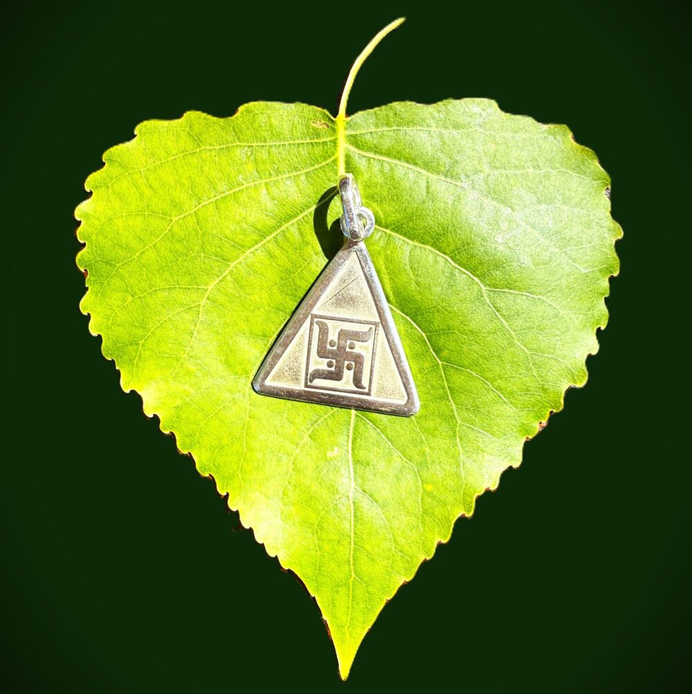 Backside of silver yantra pendant with embossed Swastik symbol on green leaf, emerald green background
